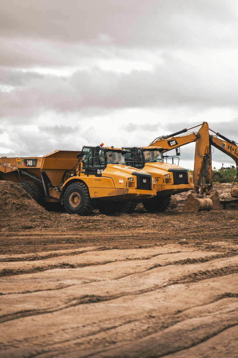 Caterpillar excavator and dump truck on a construction site with a cloudy sky.
