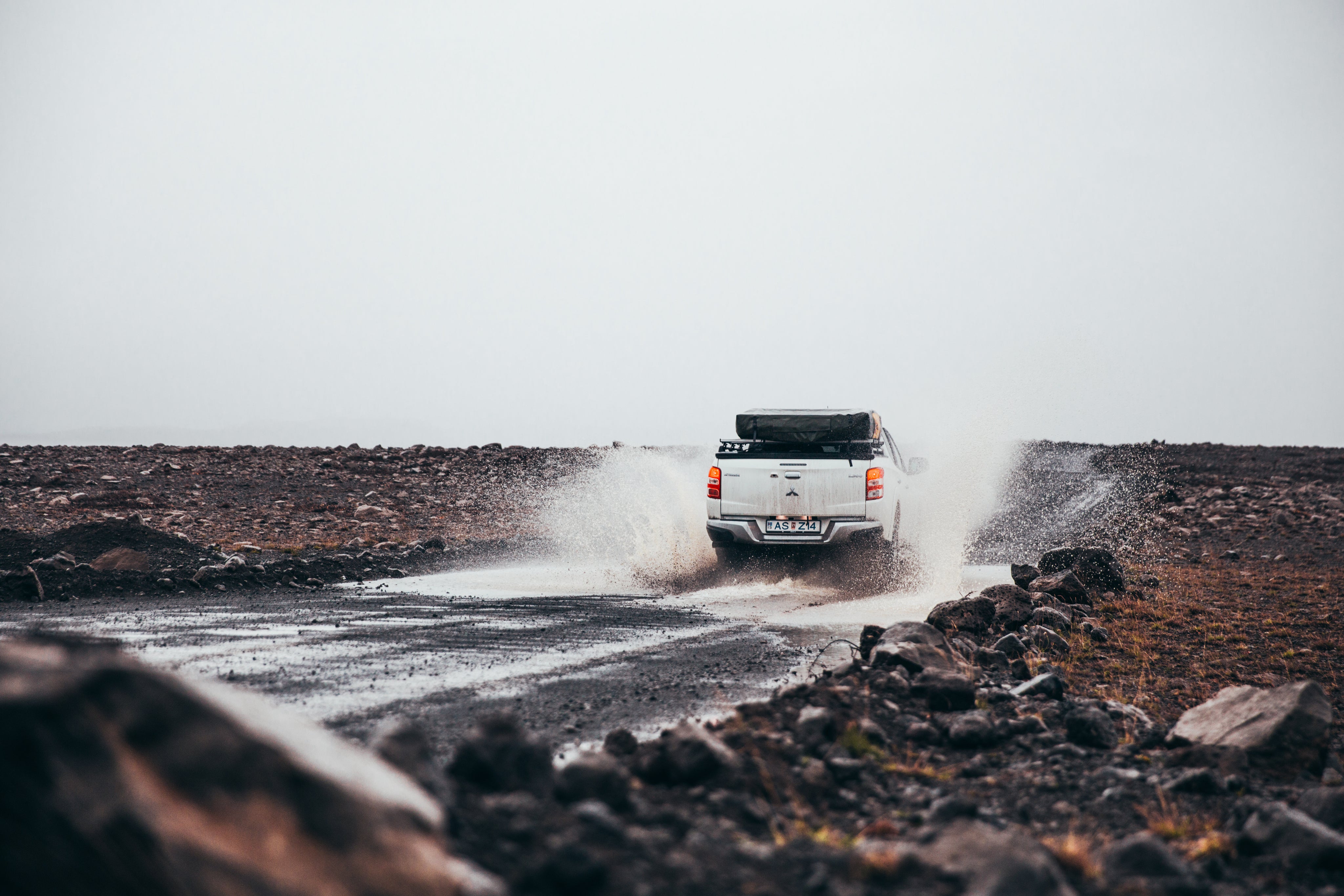 Construction truck driving down a dirt road splashing through water.